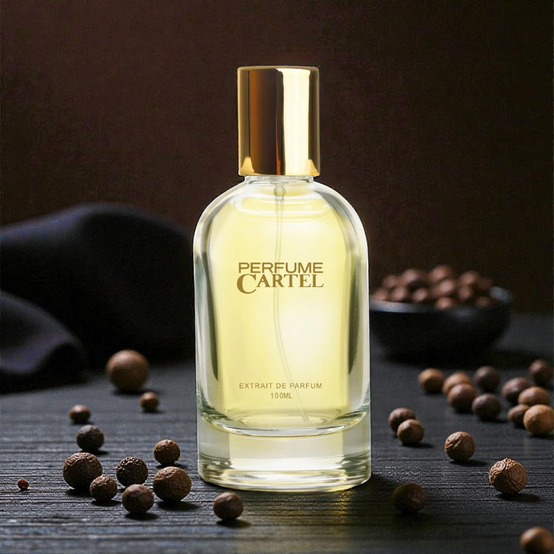Perfume Cartel bottle with gold cap on a dark surface with nuts